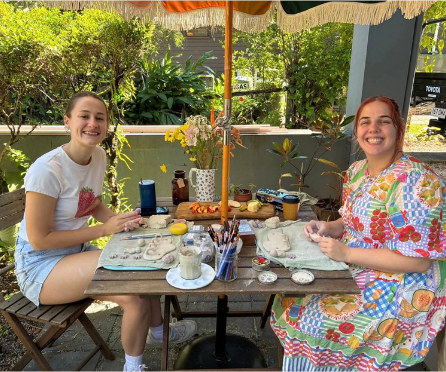 Two students hand building pottery at an outdoor table