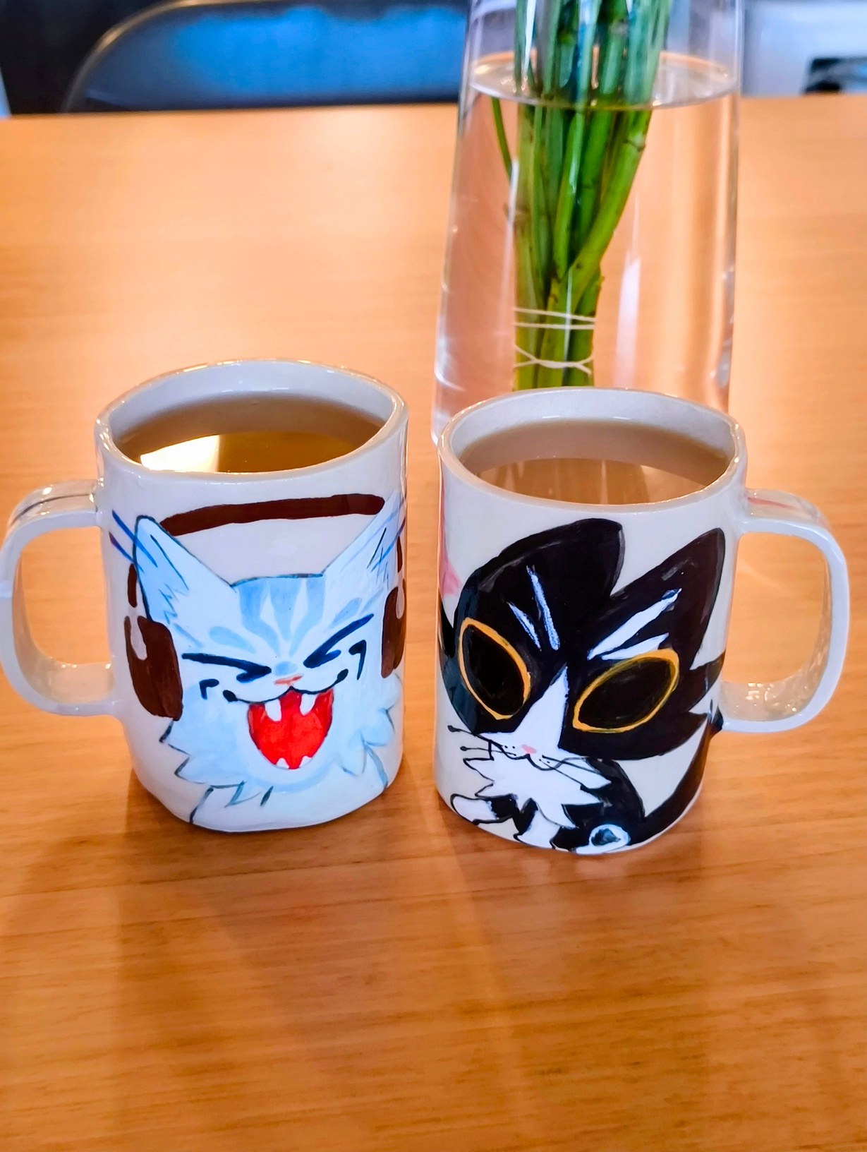 Two hand-painted cat mugs filled with tea